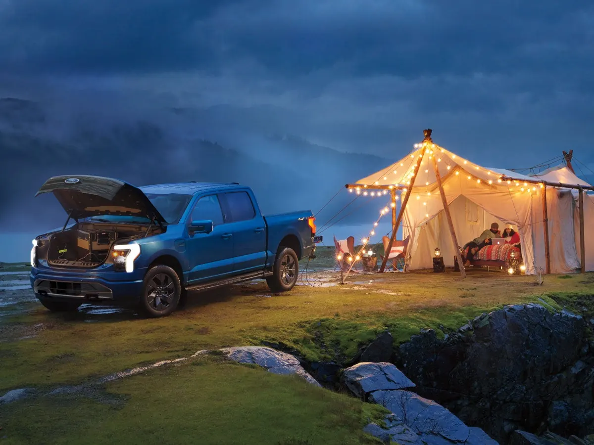 Blue F-150 Lightning powering a lit campsite tent at dusk with Pro Power Onboard