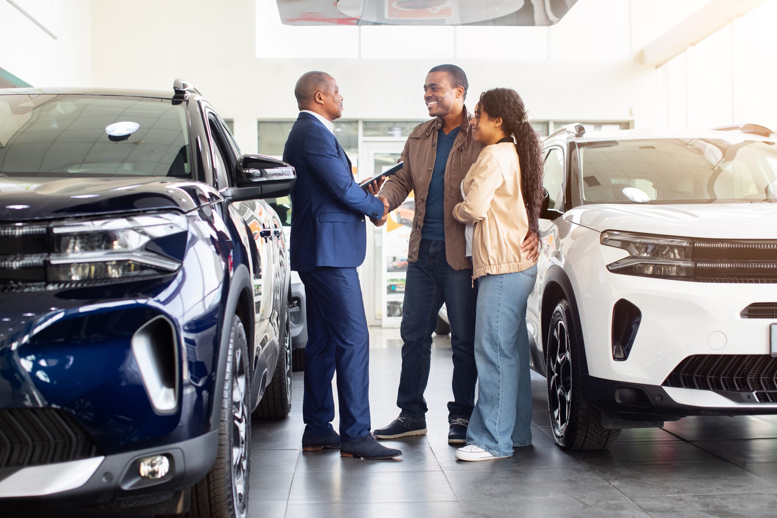 African American couple shaking hands with car dealer in showroom