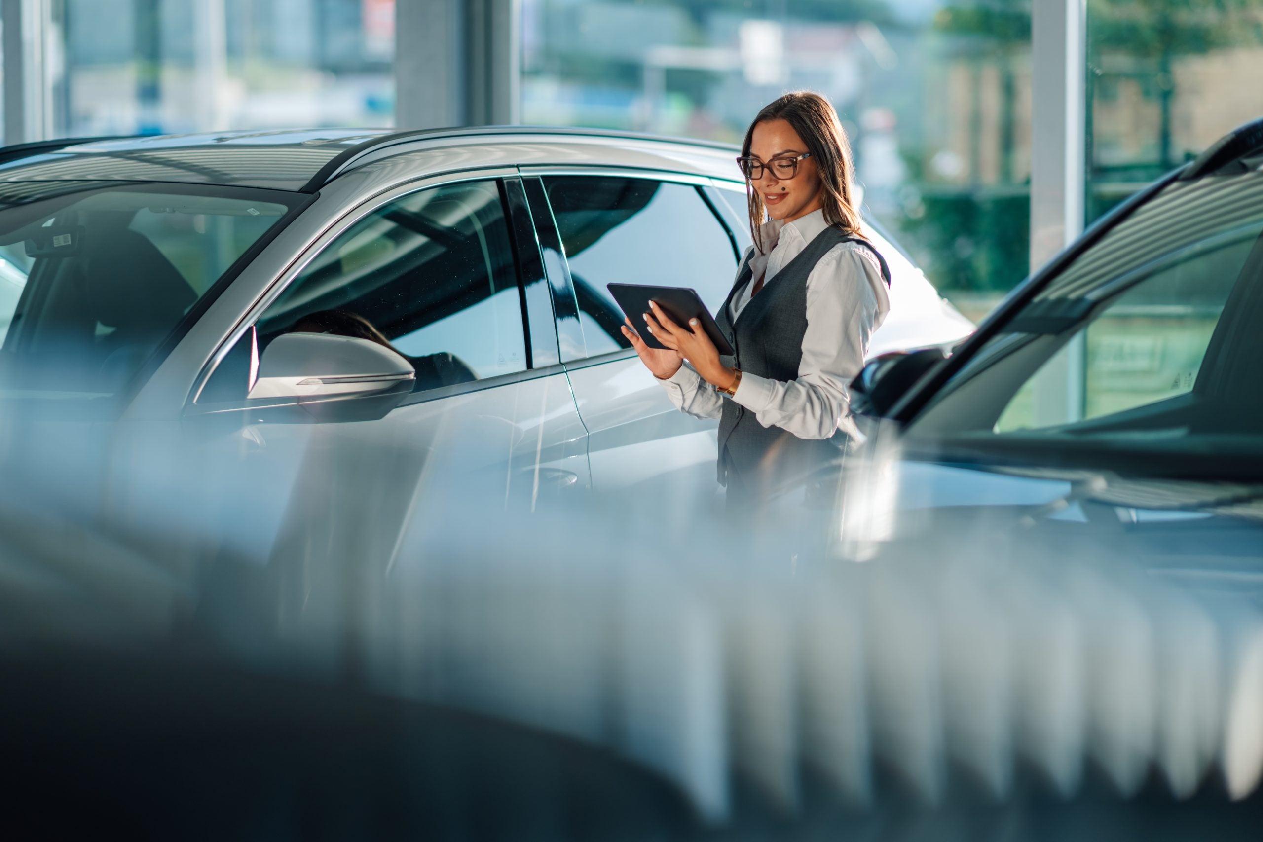 Woman utilizing a tablet to assess cars in dealership showroom