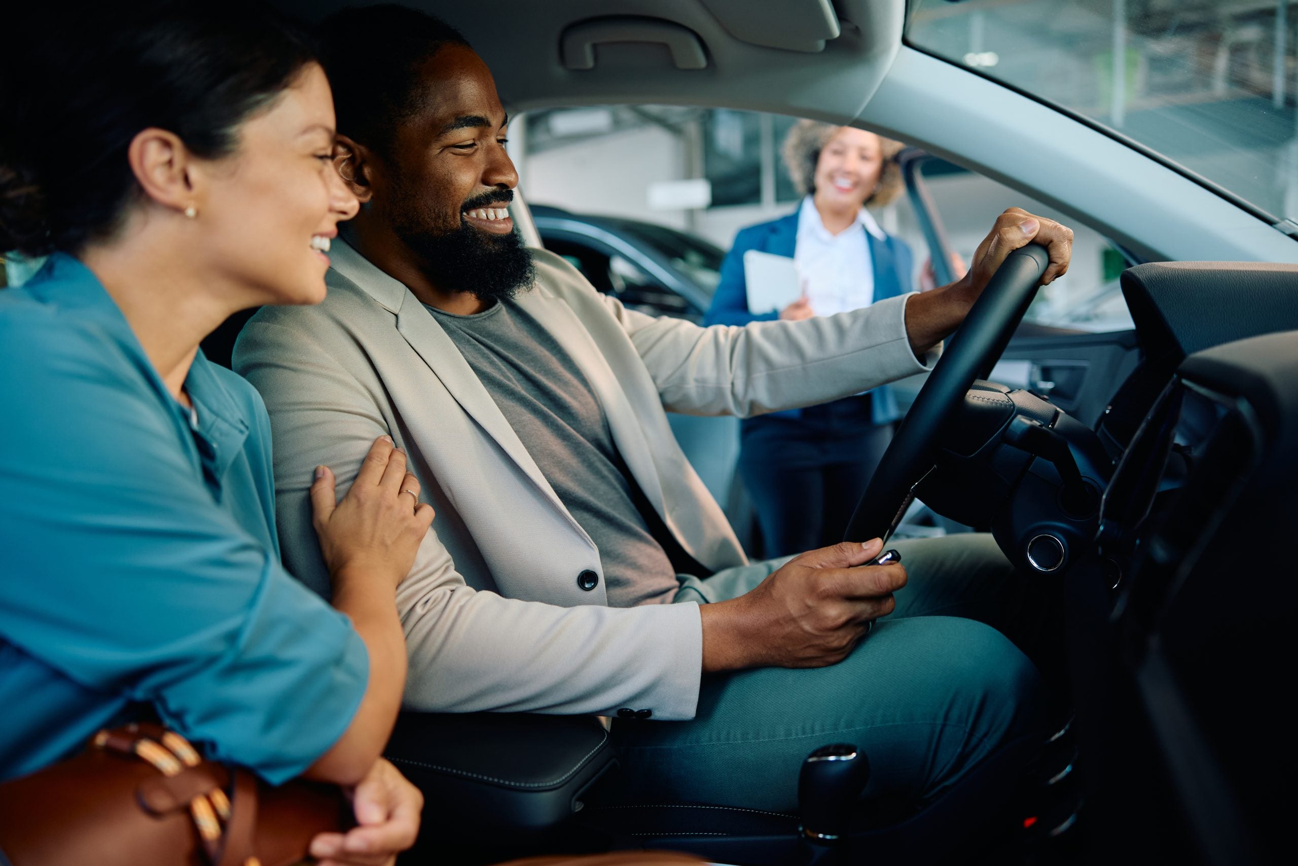 Happy multiracial couple testing new car in showroom.