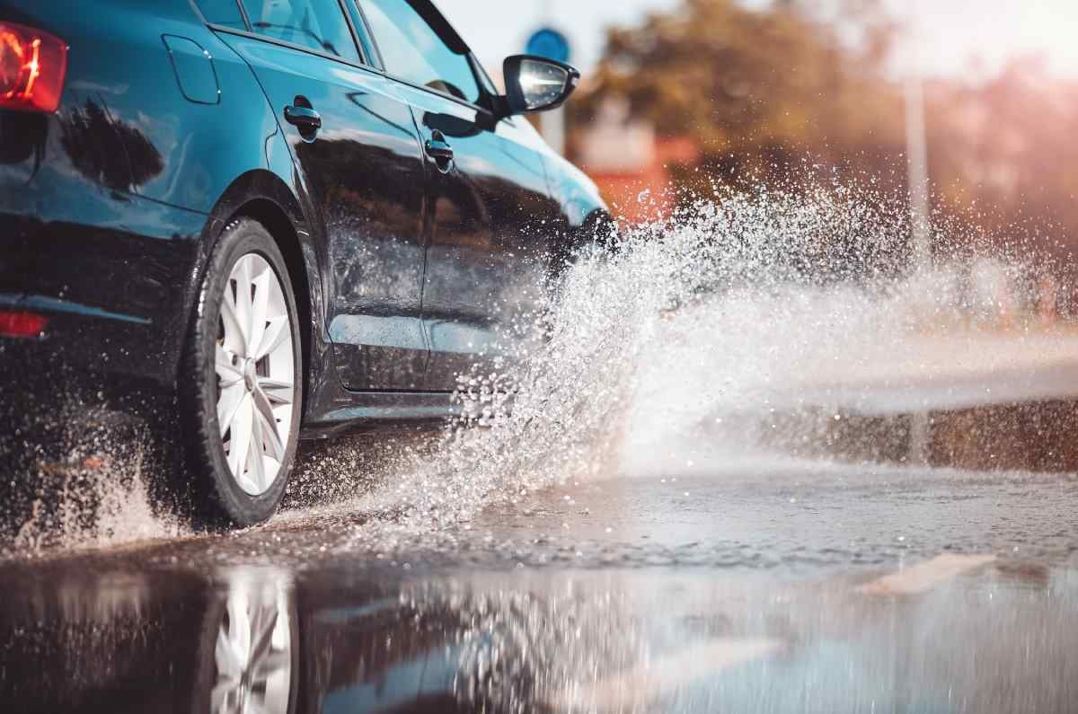A new SUV effortlessly splashes through a large puddle in the road