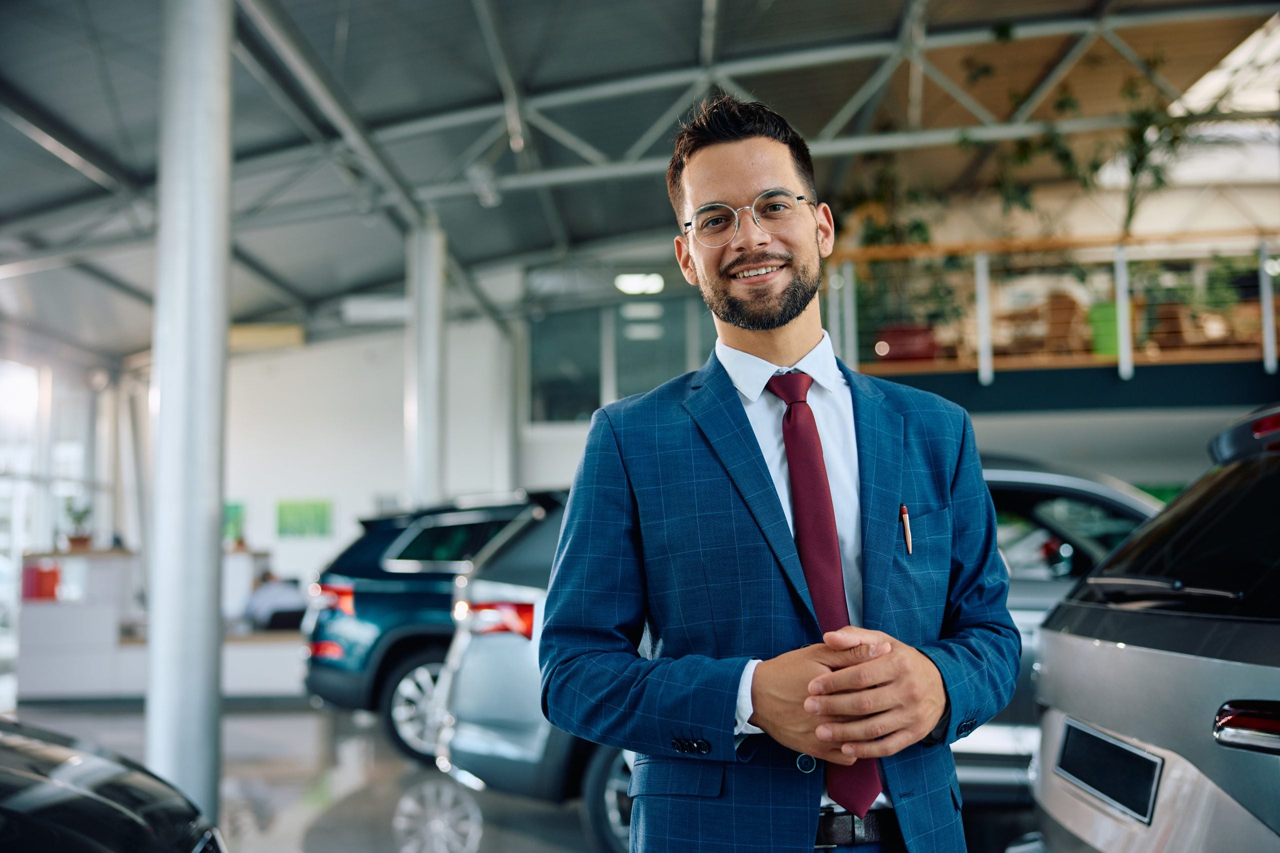 Happy salesman standing in auto salon and looking at camera.