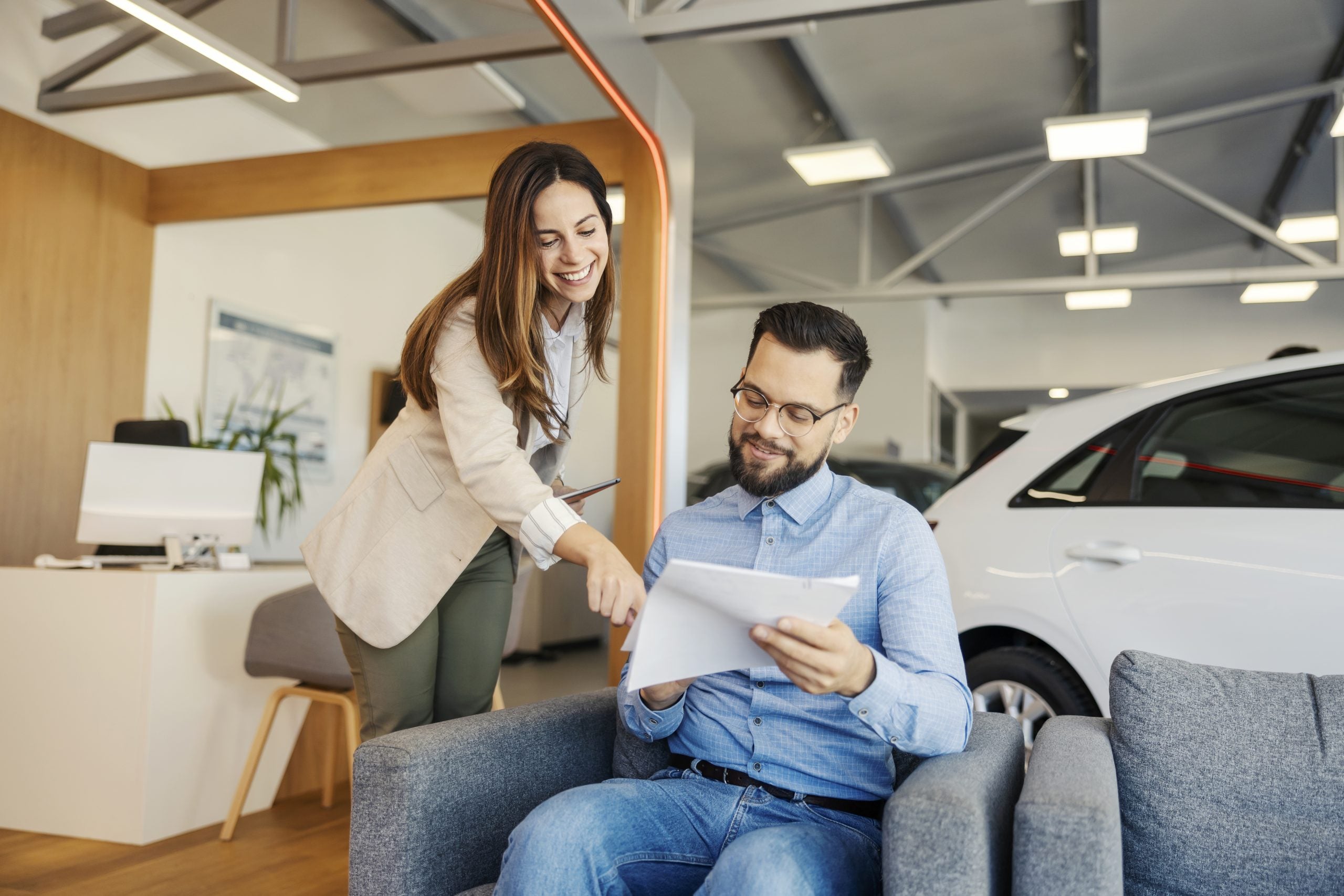 Portrait of friendly car dealer standing at car showroom and pointing at clause in contract while having talking to a buyer.