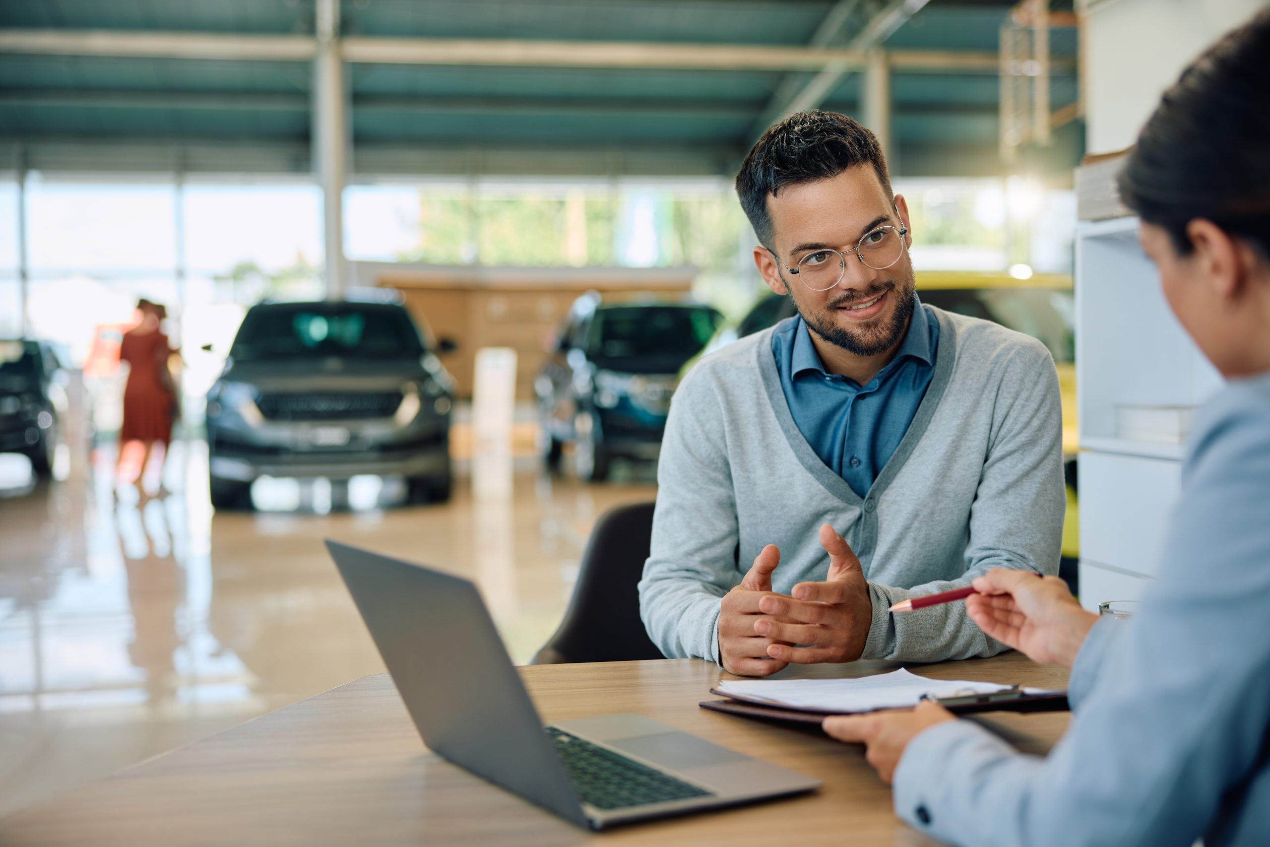 Young man discussing about terms of an agreement with car saleswoman in a showroom.