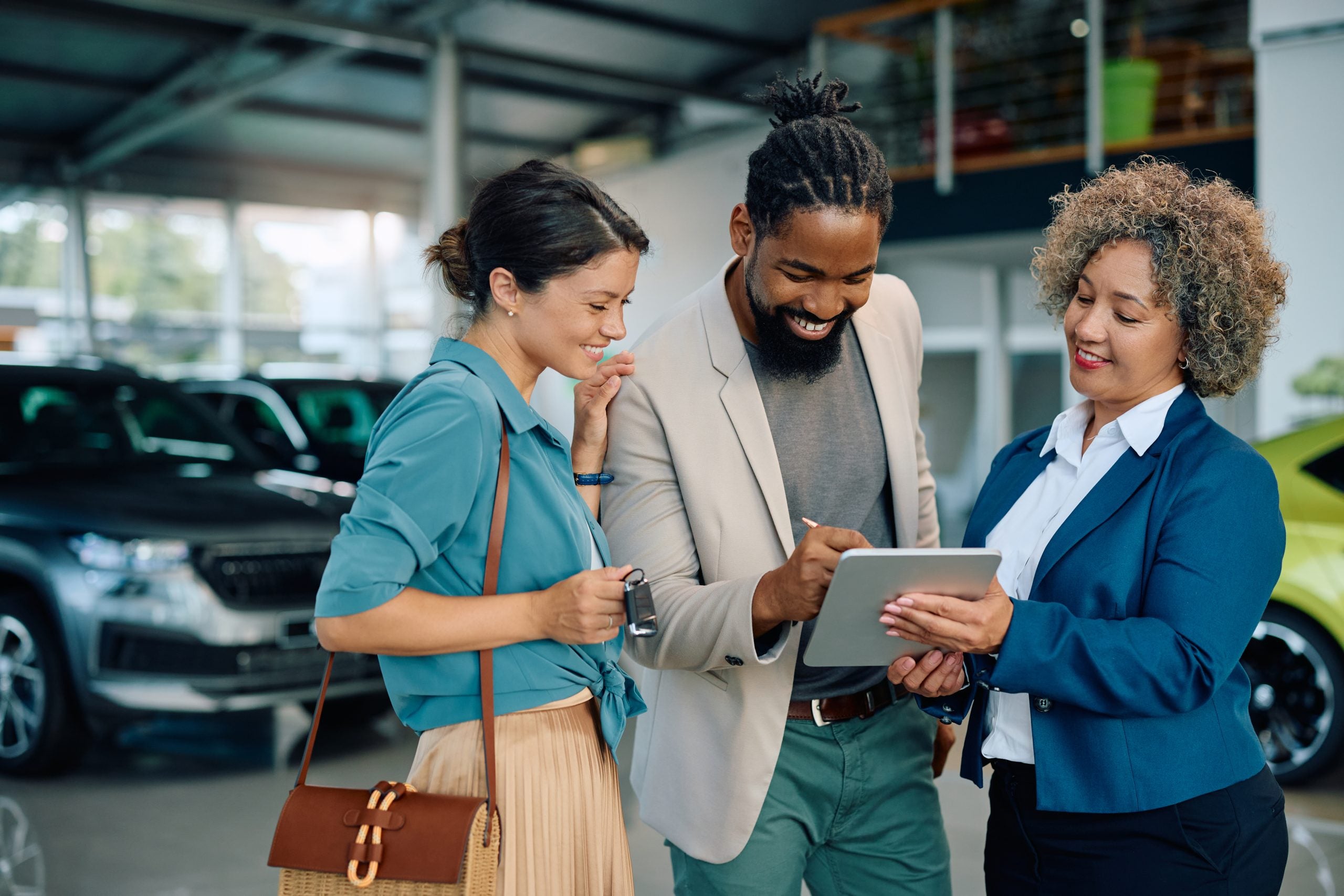 Happy couple signing an agreement on touchpad while buying new car in showroom.