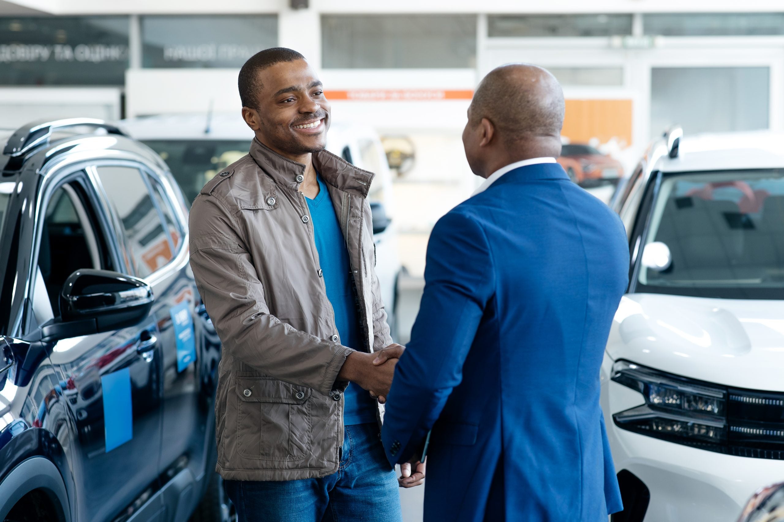 Smiling Car Seller Shaking Hands With Client After Successful Deal, Happy African American Man Buying New Vehicle In Dealership Center, Making Agreement With Salesperson In Modern Auto Showroom