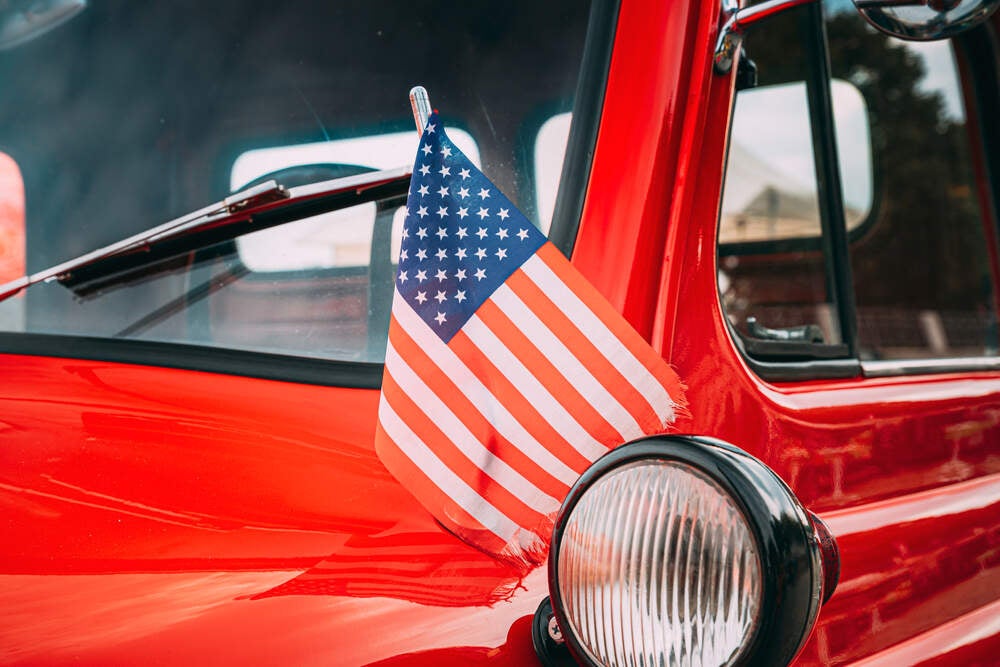 Close-up of a red truck with an American Flag on the hood