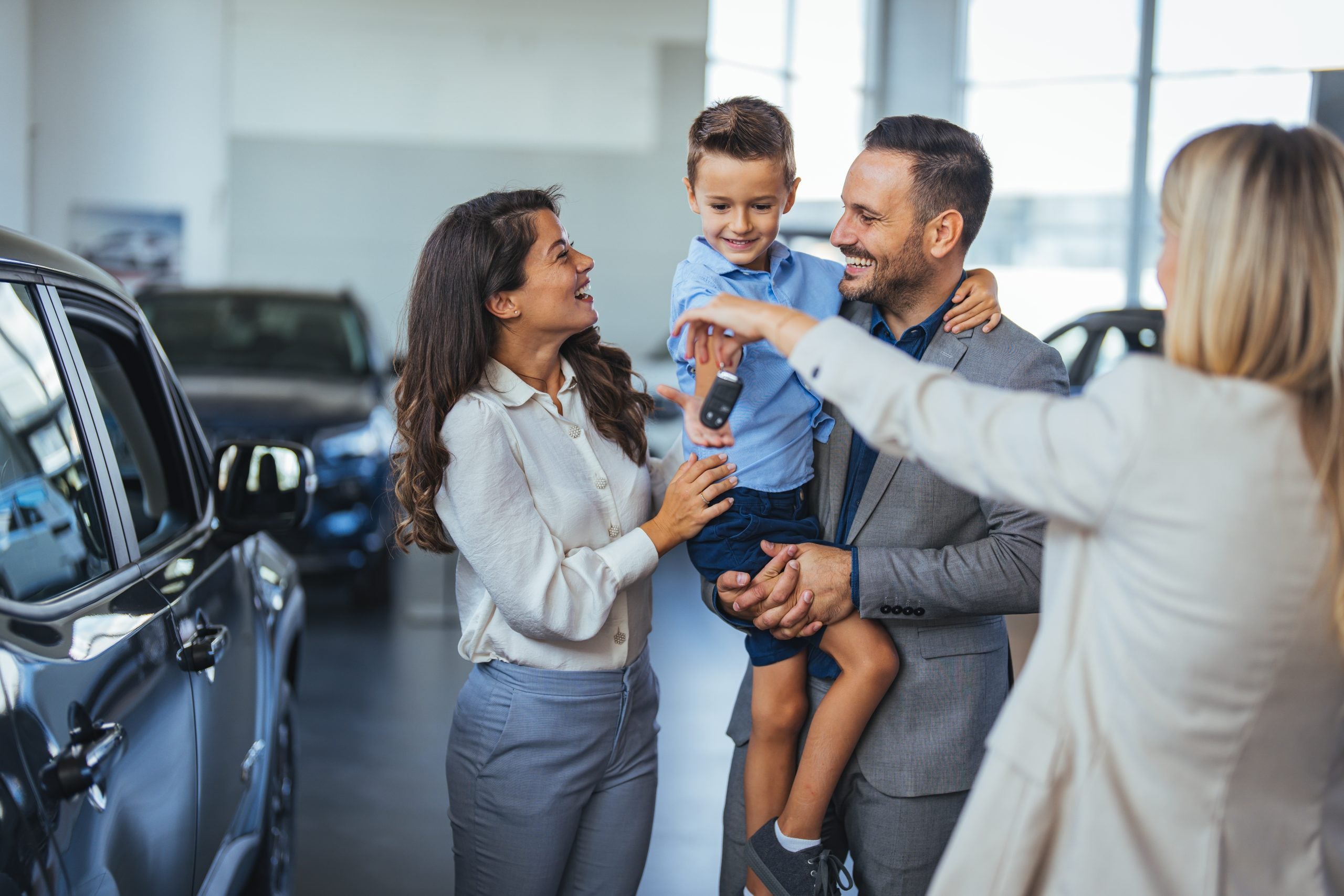Happy family holding the keys of their new car at the dealership.