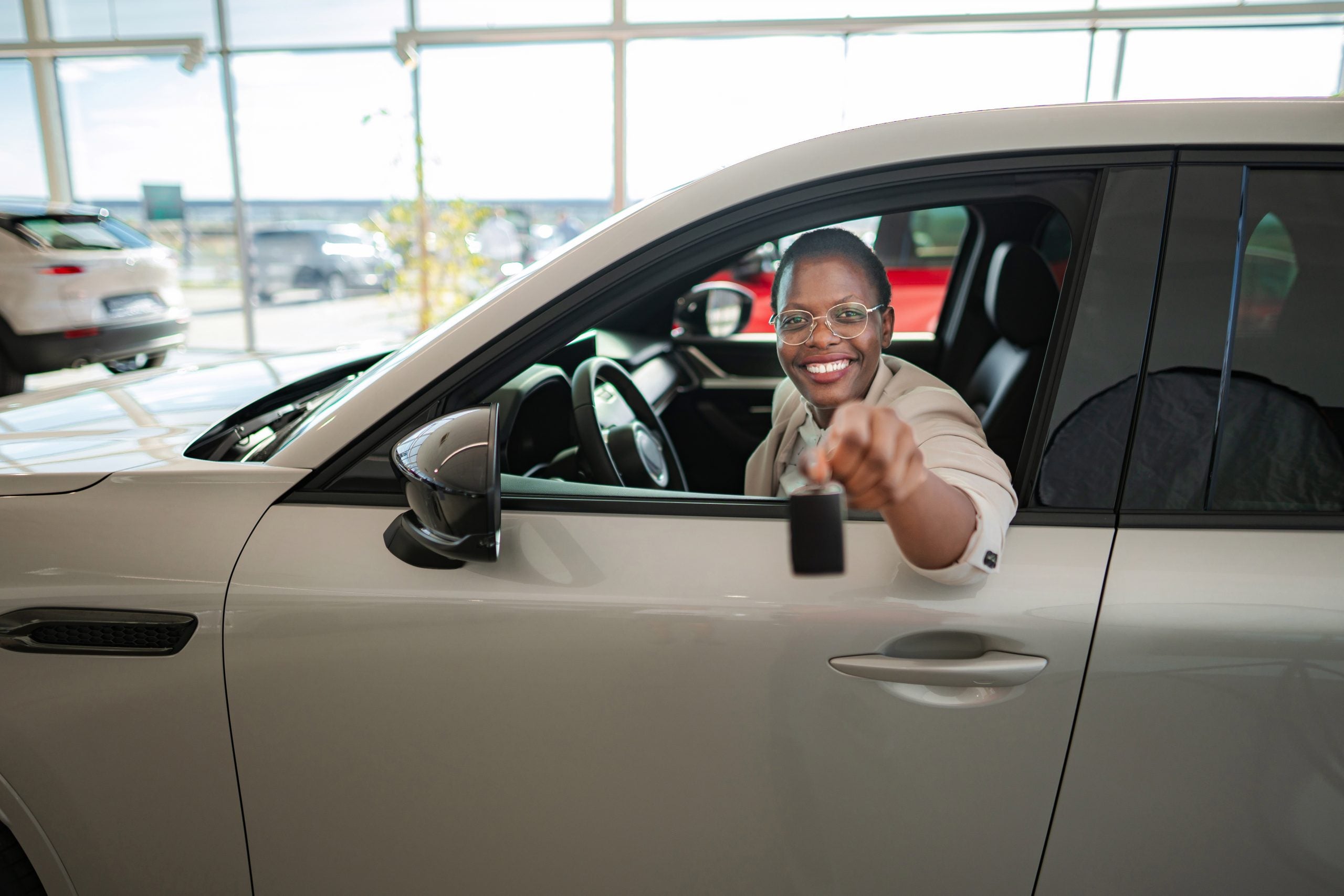 Happy woman showing new car key at dealership