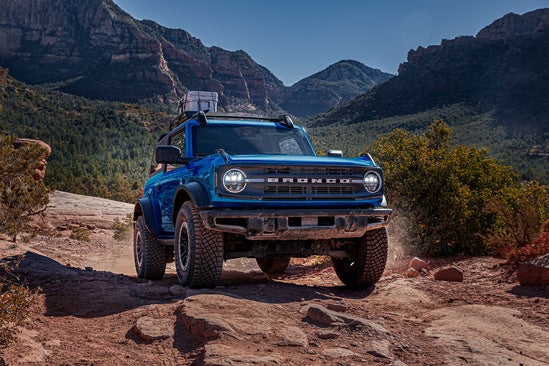 a blue 2024 ford bronco sits on top of a rocky landscape with greenery in the background 