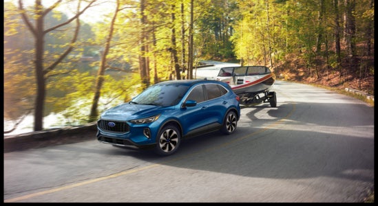 a blue ford escape towing a boat through a forest highway 
