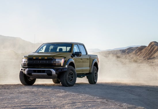 a hunter green ford f-150 driving through a dusty landscape 