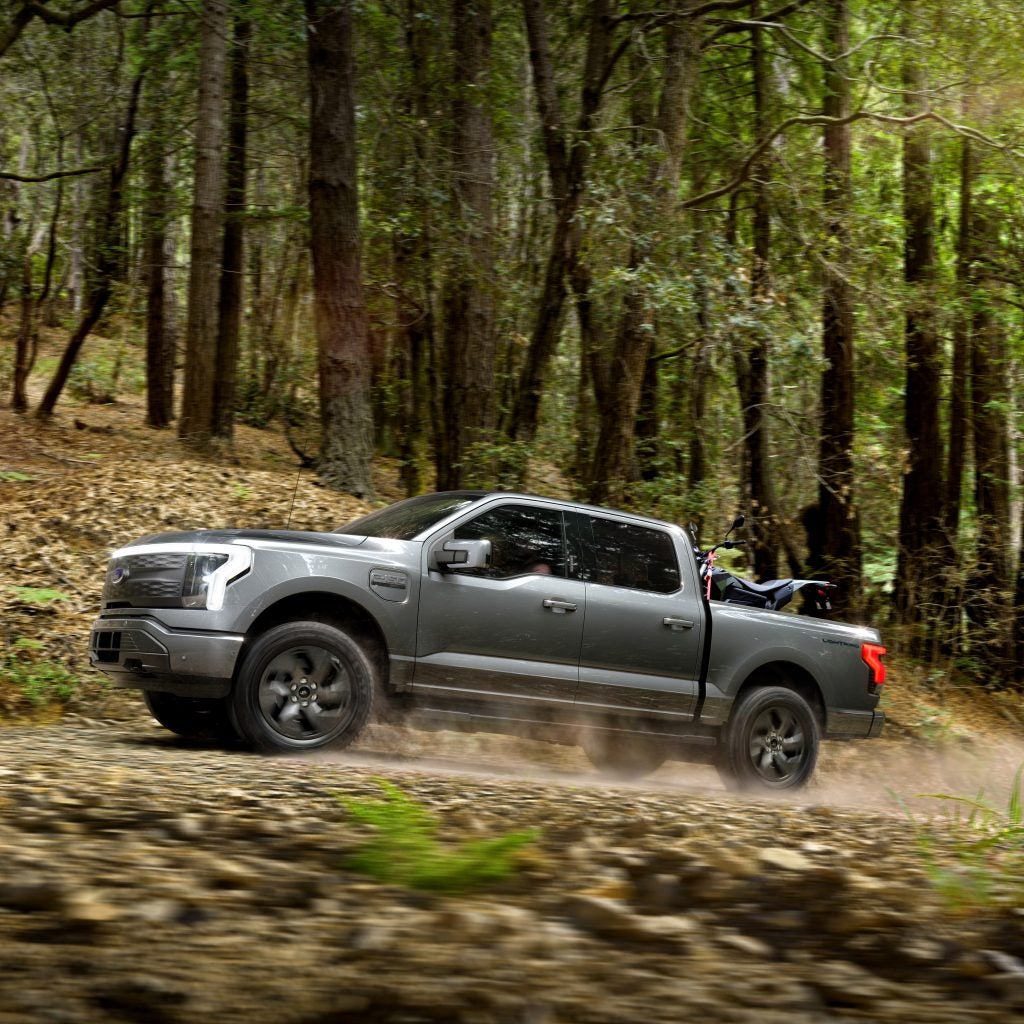A 2022 Ford F-150 Lightning driving rapidly up a wooded mountain road in Joplin Missouri