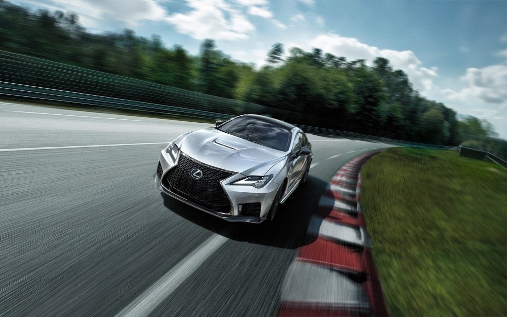 An all-new silver 2025 Lexus RC-F speeding on a race track to the finish. - Lexus of Huntsville, AL