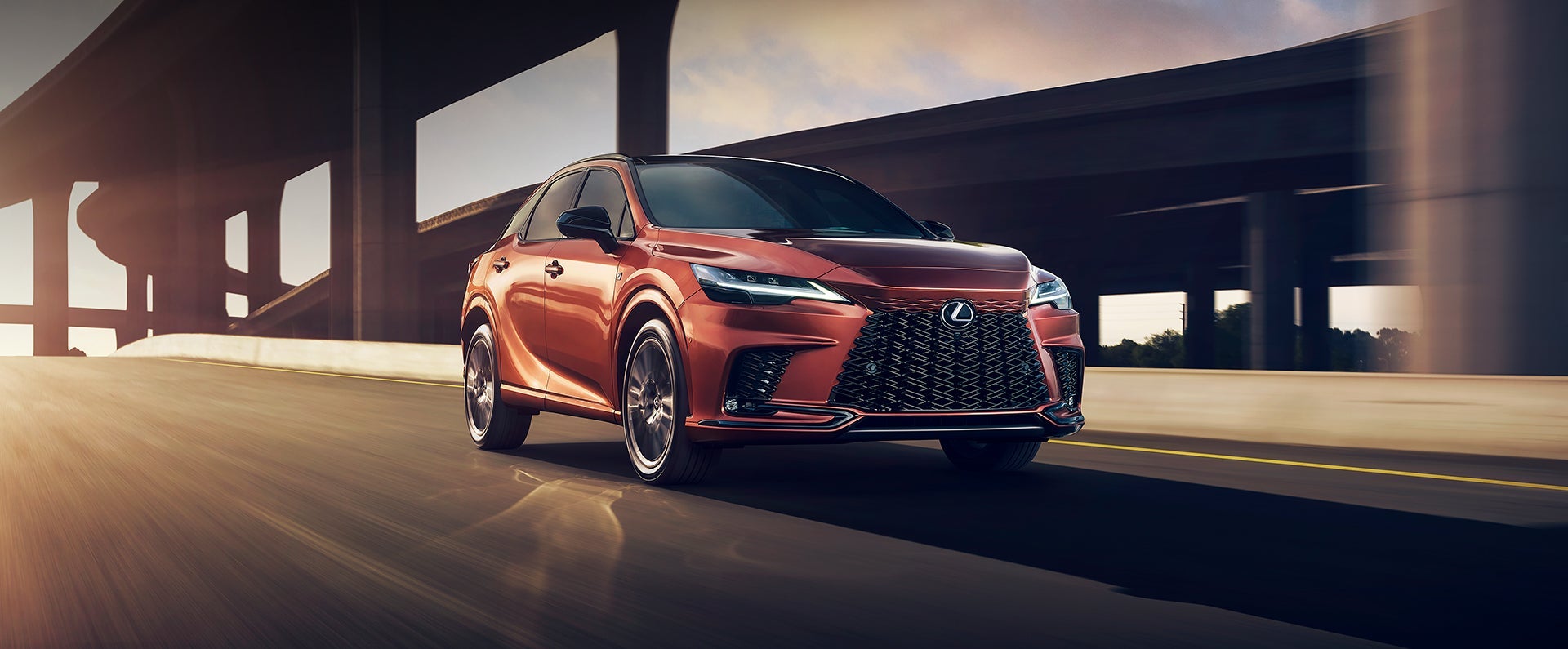 A photo of an orange 2024 Lexus RX driving down a city street.