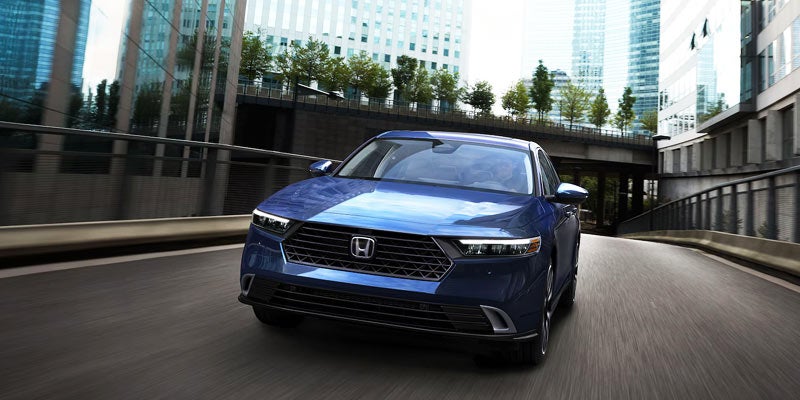 Blue Honda sedan driving through a city curve with modern buildings in the background.