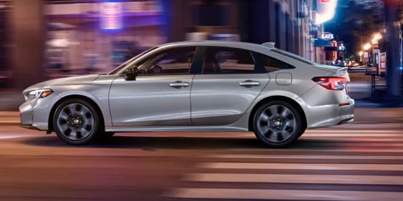 Silver sedan driving through a city street at night with motion blur and urban lights.