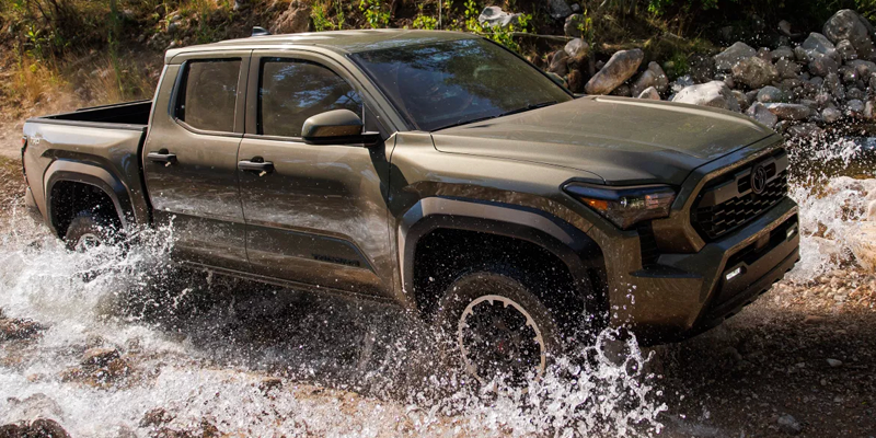 Olive green pickup truck driving through shallow river crossing