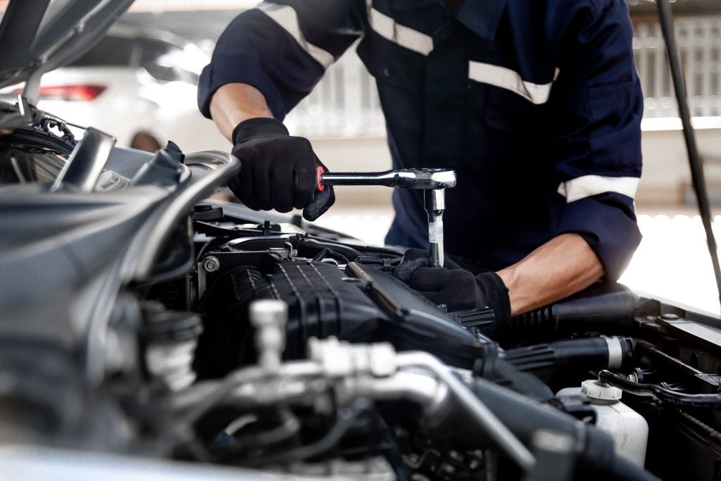 Mechanic performing vehicle engine maintenance with tools under the hood.