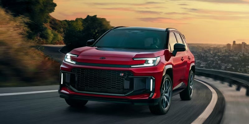 Red Toyota SUV driving on a winding road at sunset.
