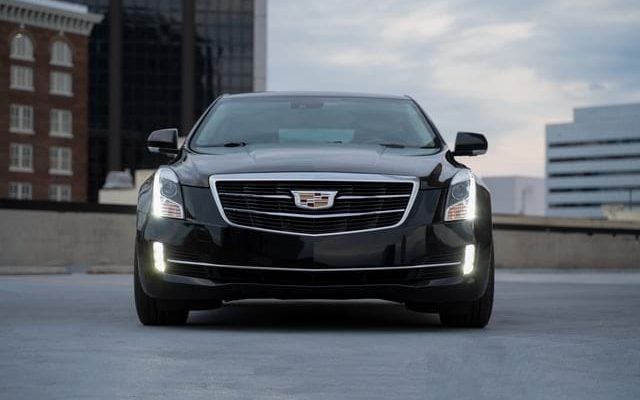 Black Cadillac car from the front on top of parking garage with lights on
