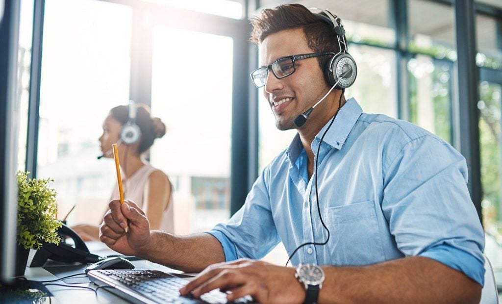 Man, and woman in background, wearing headphones and working on computers.