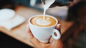 A small cup of coffee with milk being poured creating a tree shaped surface