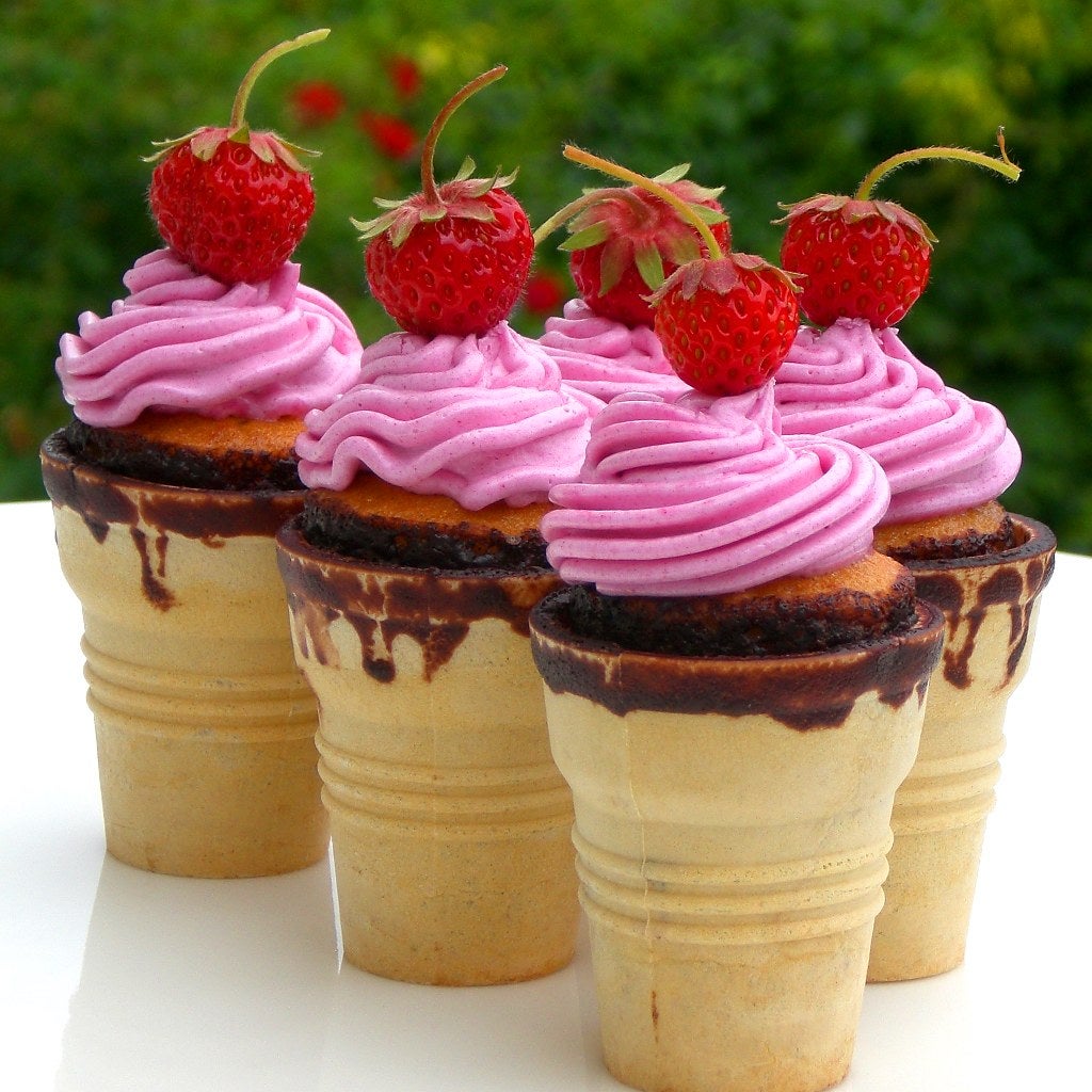 Filled ice cream cones with what looks like with frosting with a raspberry on top of each one
