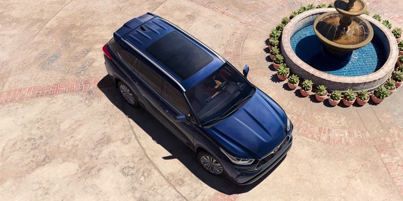 Blue SUV parked in a courtyard beside a circular fountain viewed from above.