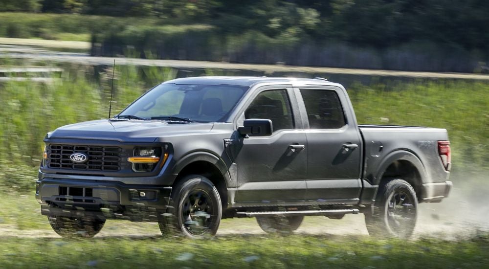A grey 2025 Ford F-150 STX FX4 driving on a dusty trail.