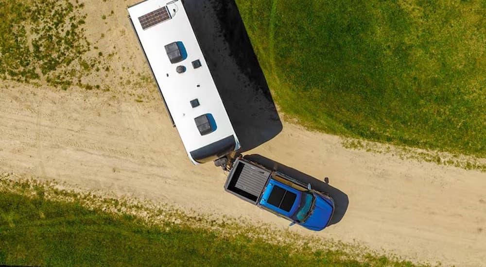 Blue 2025 Ford F-150 XLT towing a camper on a dirt road.