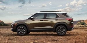 Profile view of a dark taupe 2021 Chevrolet Trailblazer parked in an open area with partly cloudy skies overhead. | Chevrolet dealer in St. Louis, MO
