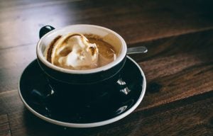 A cup of coffee topped with whipped cream in a black mug on a saucer. | St. Louis, MO