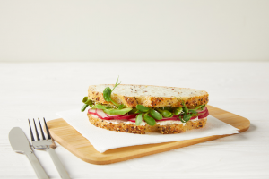 A veggie sandwich on a wooden board and a knife and fork beside it. | Eateries in St. Louis, MO