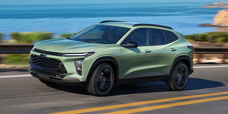An all-new 2024 Light Green Chevy Trax driving along an oceanside highway. - Ted Britt Chevrolet Sterling, VA