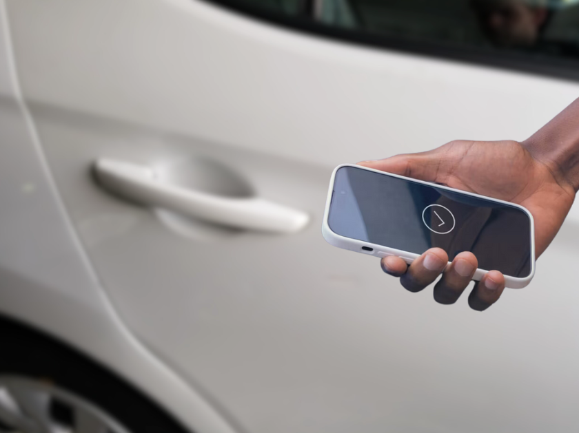 Person holding a smartphone with Hyundai Digital Key app near the door handle of a white Hyundai vehicle