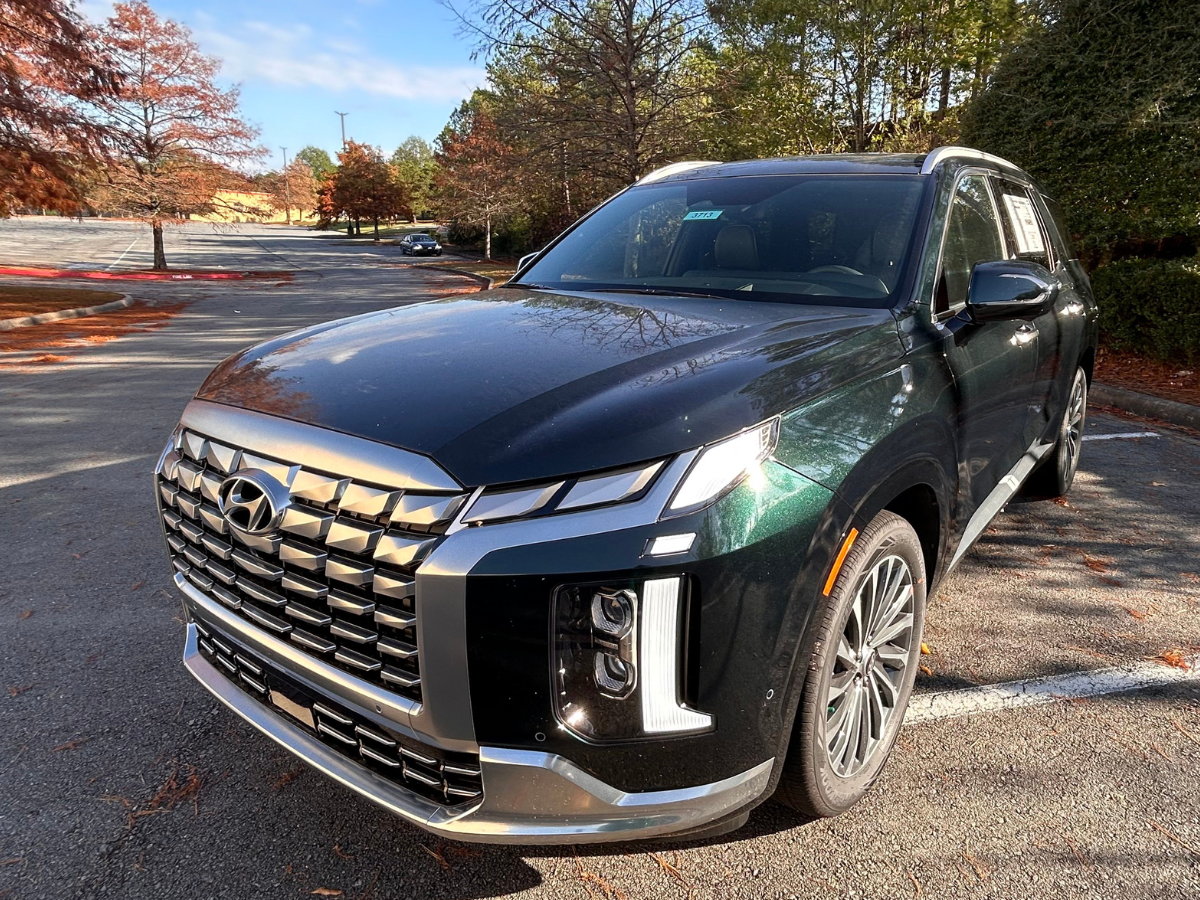 A 2025 Hyundai Palisade SUV parked outdoors in a wooded lot, showcasing its bold grille and modern LED lighting.