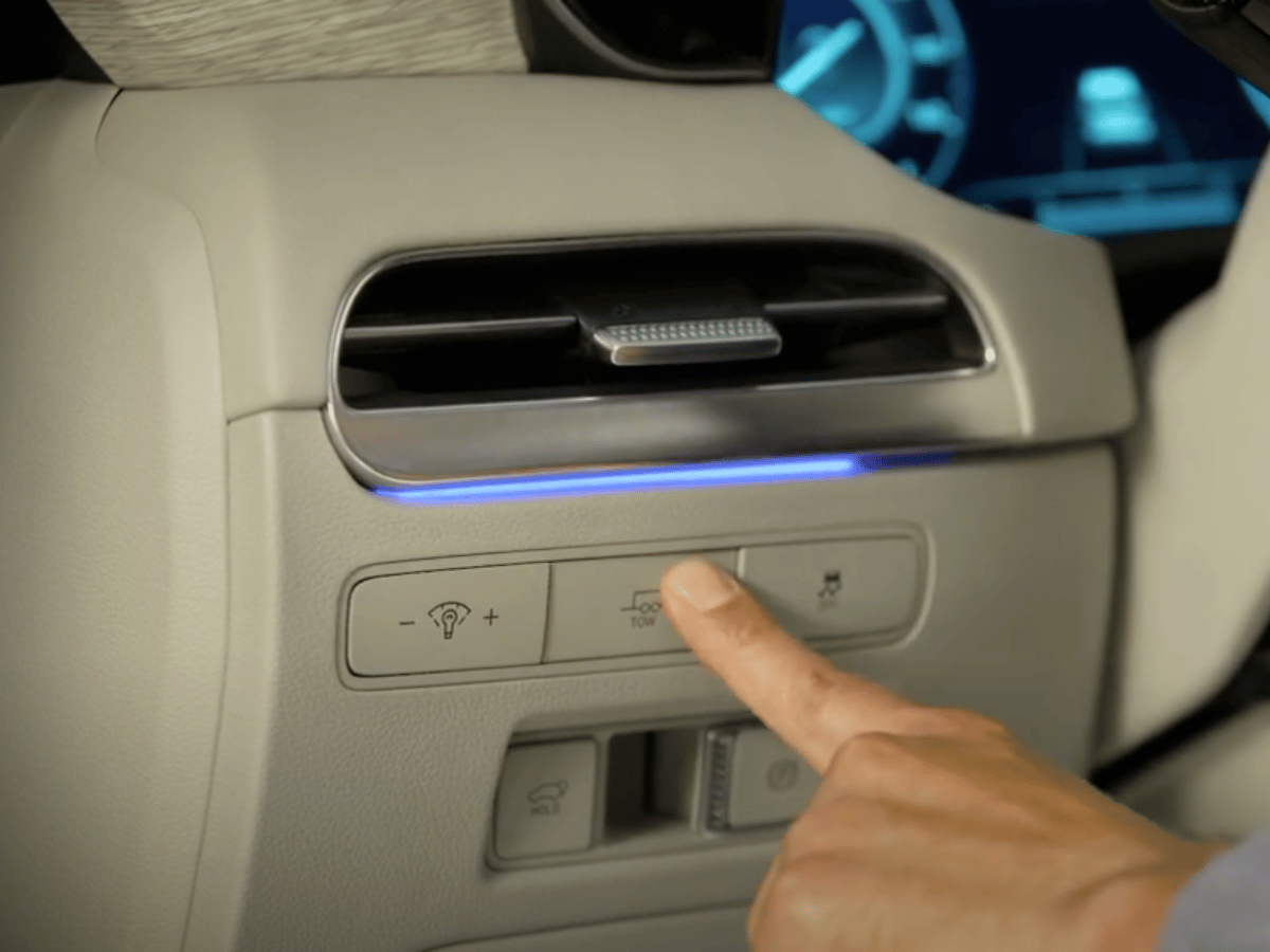 Driver pressing the Tow Mode button on the dashboard of the 2025 Hyundai Palisade, showcasing the vehicle’s advanced towing features.
