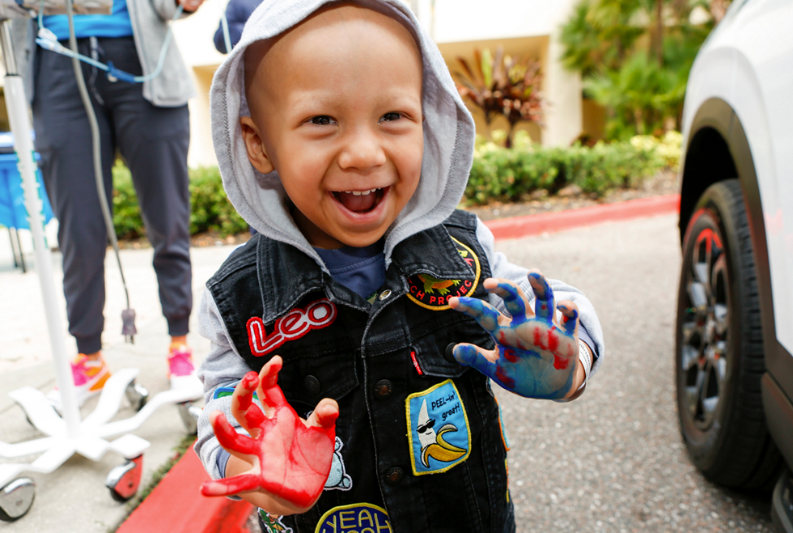 Smiling child with red and blue painted hands at a Hyundai Hope On Wheels event