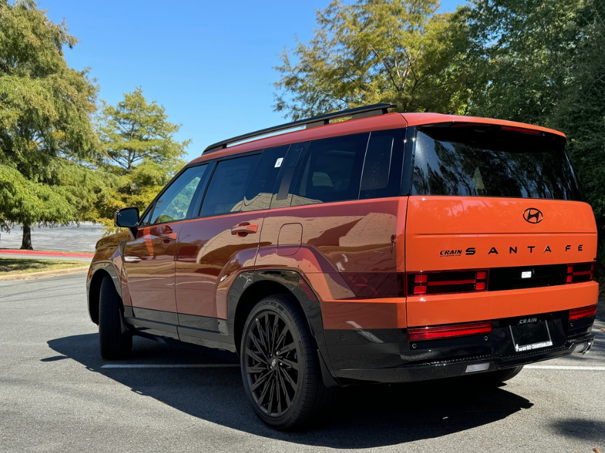 Rear and side view of a 2025 Hyundai Santa Fe in Terrain Orange parked under fall trees in Little Rock, Arkansas