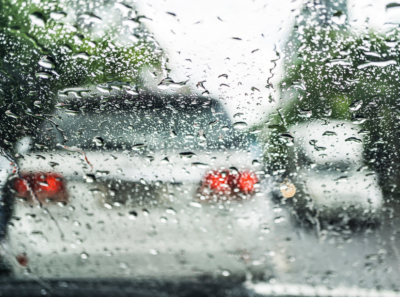 Rain-covered windshield with blurred cars and taillights on a stormy day
