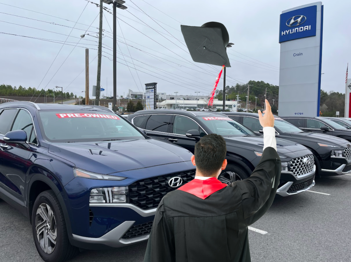 Graduate celebrating in front of pre-owned Hyundai vehicles at Crain Hyundai dealership