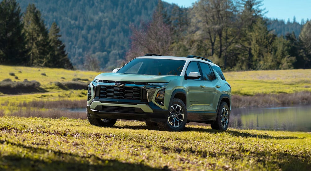 A green 2025 Chevy Equinox ACTIV parked on grass near a pond.