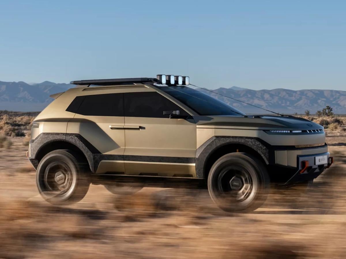 Profile view of the gold Hyundai CRATER Concept EV SUV driving through a desert landscape, featuring 33-inch off-road tires, a rugged roof rack with pixel lights, and limb riser cables.