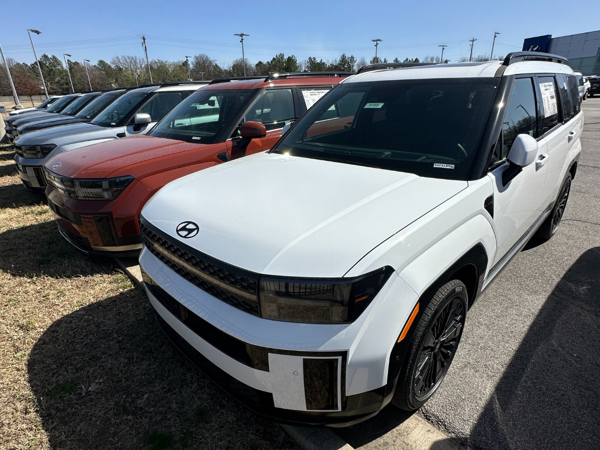 Row of new Hyundai SUVs, including Palisade and Santa Fe models, parked at Crain Hyundai of Fayetteville under clear skies.