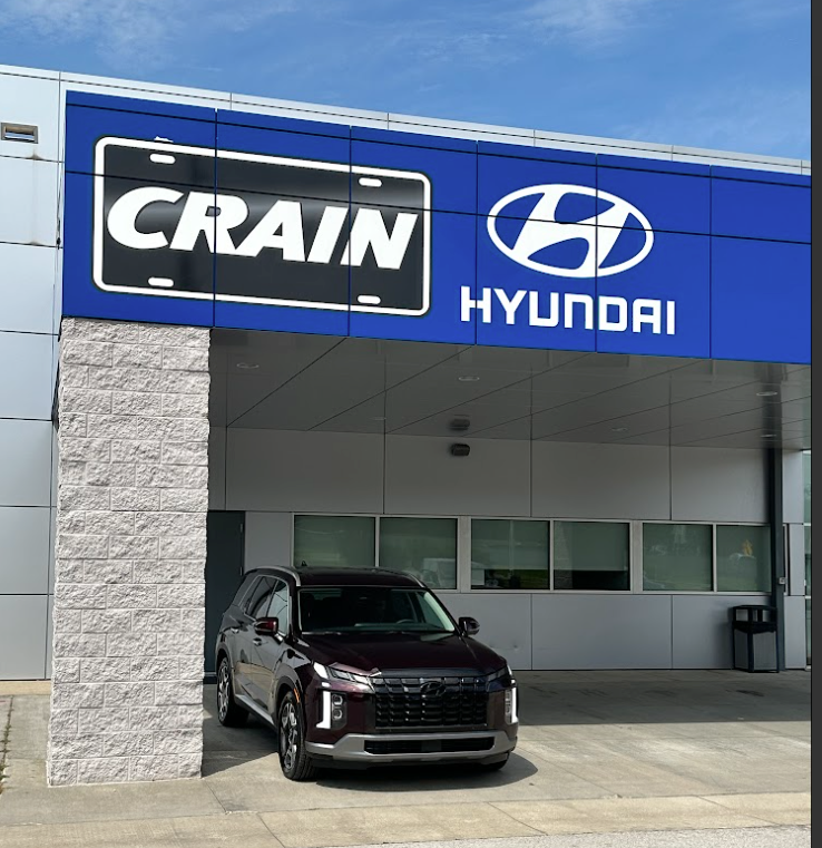 A maroon Hyundai SUV parked beneath the Crain Hyundai Fayetteville dealership awning.