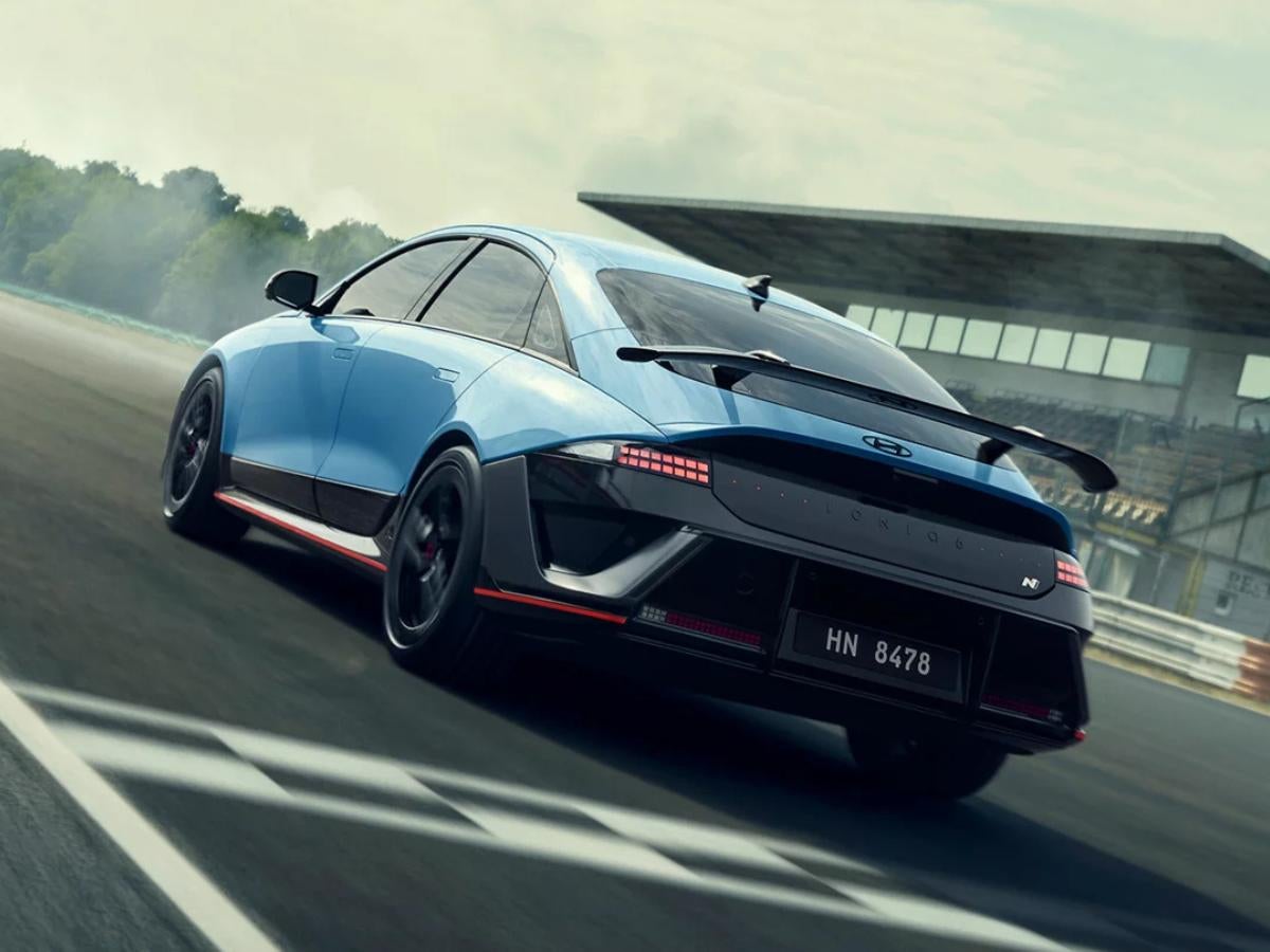 Rear view of the 2026 Hyundai IONIQ 6 N in Performance Blue speeding on a racetrack, highlighting its swan-neck rear wing and dual-layer diffuser.