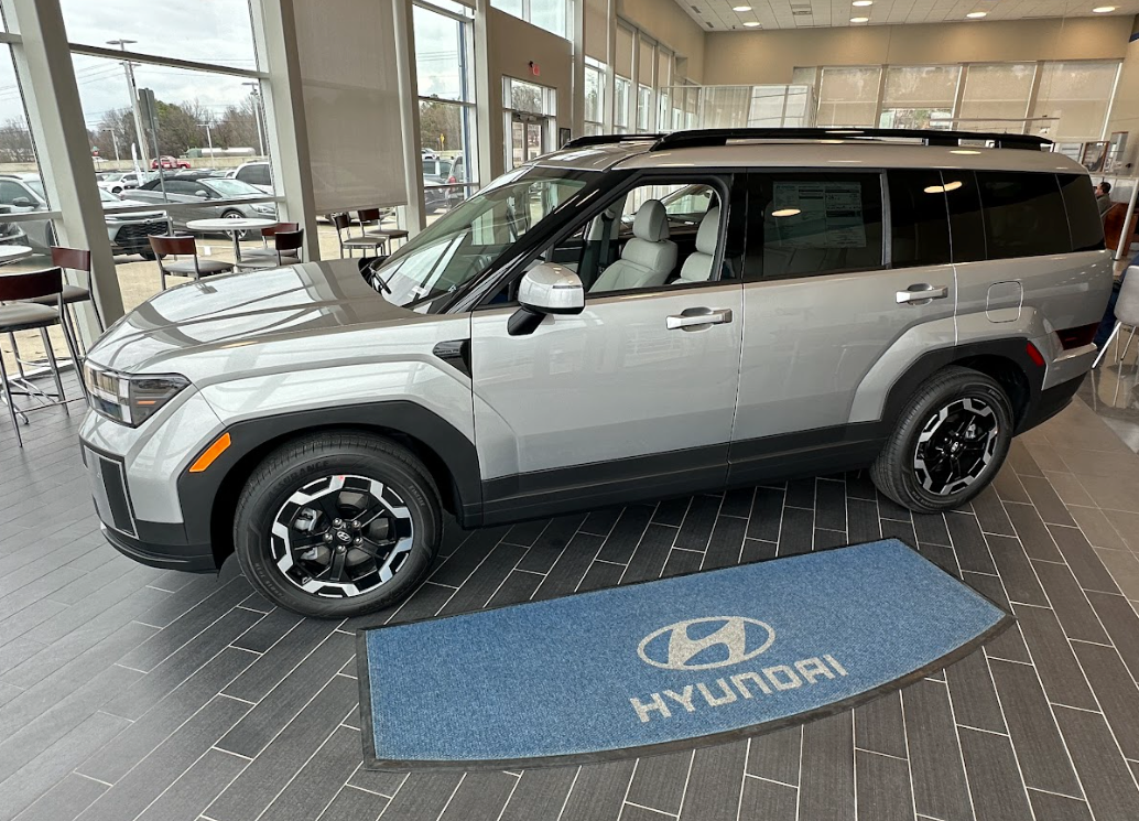 Silver Hyundai SUV parked inside showroom on a Hyundai logo mat, with bright windows in the background