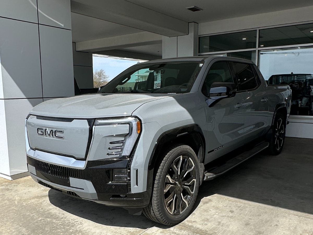 Front and side view of the 2026 GMC Sierra EV pickup truck in gray, parked at Crain Buick GMC in Springdale, Arkansas