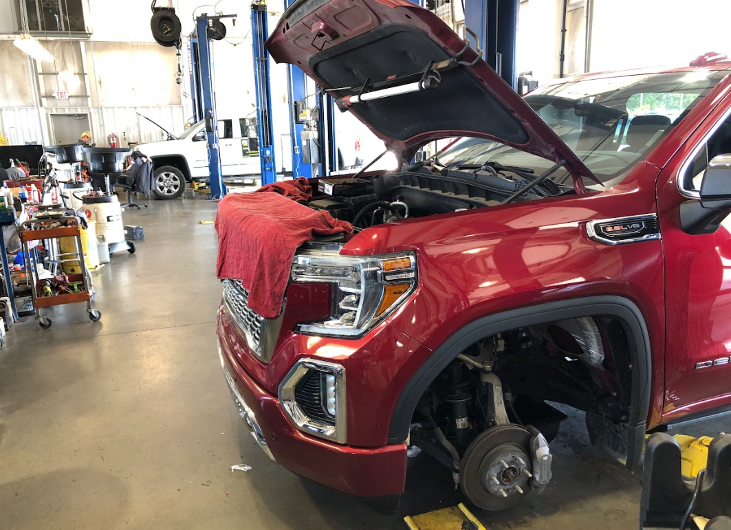Red GMC truck undergoing service at Crain Buick GMC in Springdale with hood open and tire removed